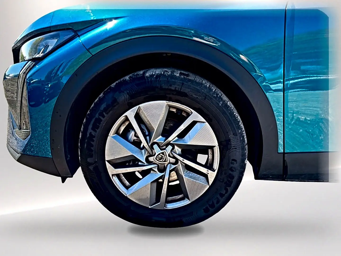 Gros plan sur la roue avant gauche bleu métallisé d'une Peugeot 408 Hybrid 145 allure avec jante alu au design moderne.