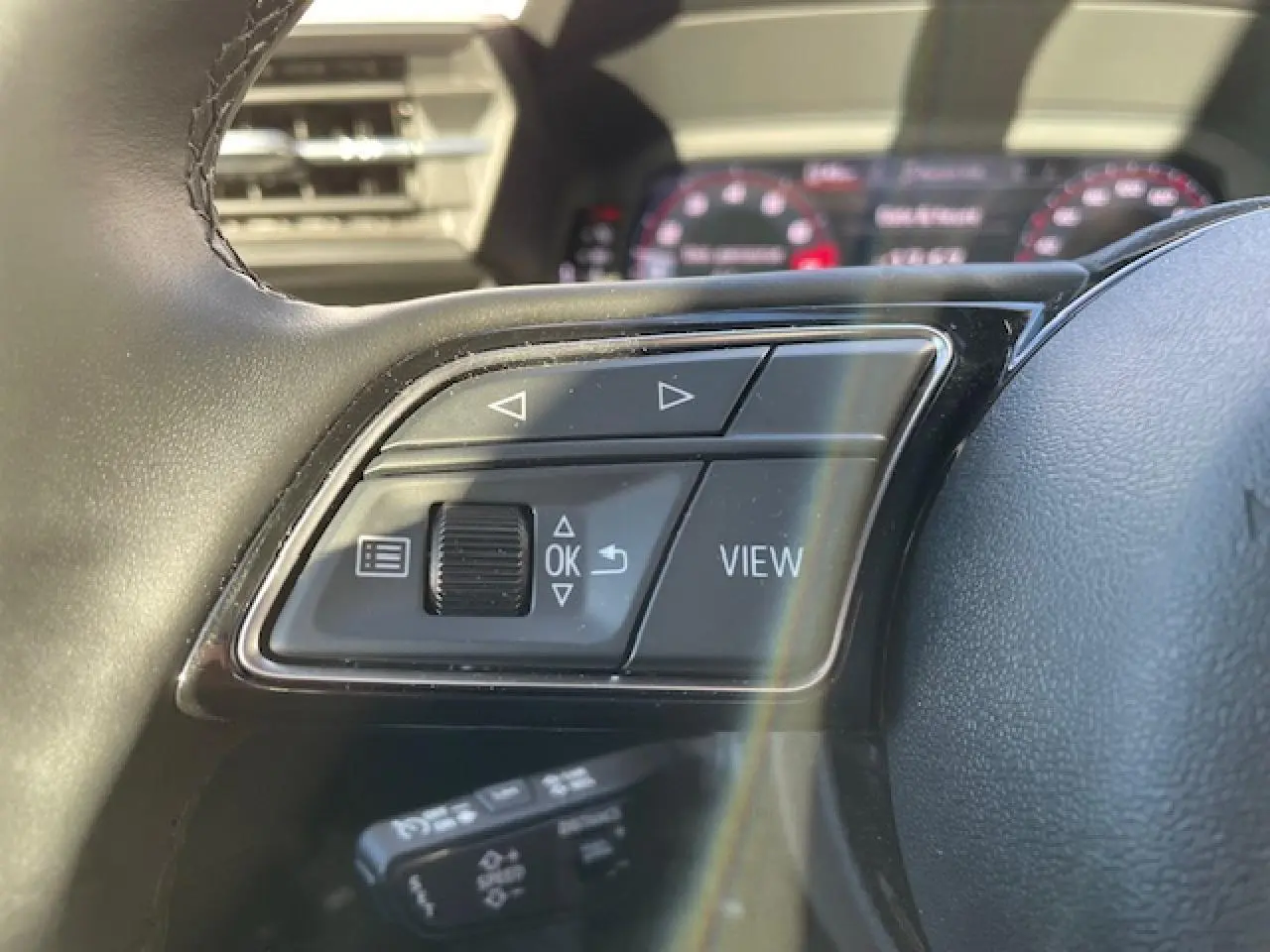 Gros plan sur les commandes au volant de l'Audi A3 2022, finition confort, tableau de bord digital en arrière-plan flou.