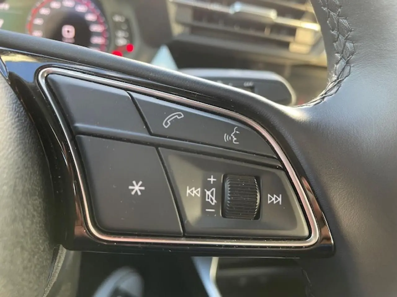 Gros plan sur les commandes du volant en cuir noir de l'Audi A3 IV Berline 30 TFSI MHEV argent métallisé, avec tableau de bord flou.