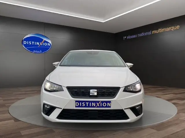Vue frontale d'une SEAT IBIZA 1.0 MPI 80 STYLE blanche Candy avec phares allumés dans un showroom.