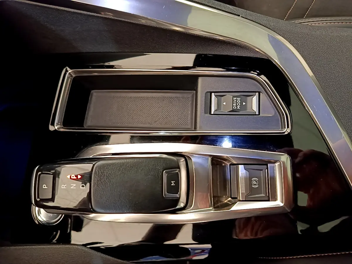 Gros plan sur la console centrale noire brillante du Peugeot 3008 rouge, avec levier de vitesses automatique et bouton Drive Mode.