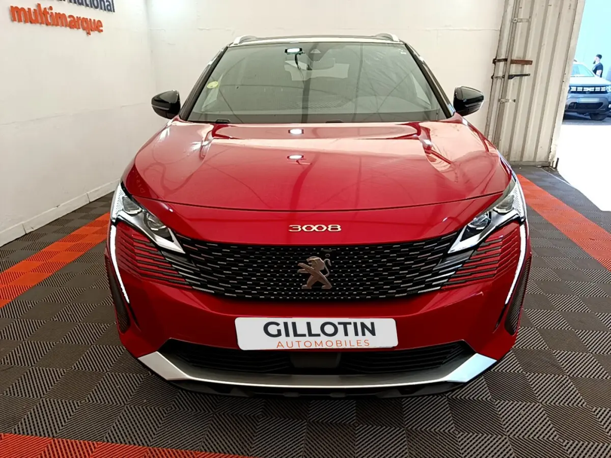 Vue frontale d'un Peugeot 3008 rouge avec calandre noire et logo lion au centre, en intérieur showroom.
