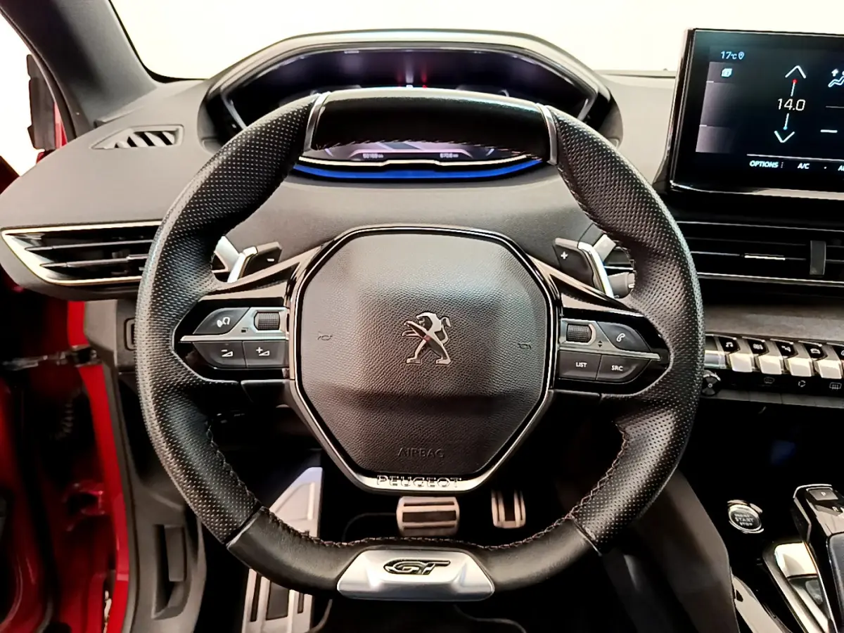 Vue rapprochée du volant cuir noir GT du Peugeot 3008 rouge 2021 avec tableau de bord digital et écran tactile.