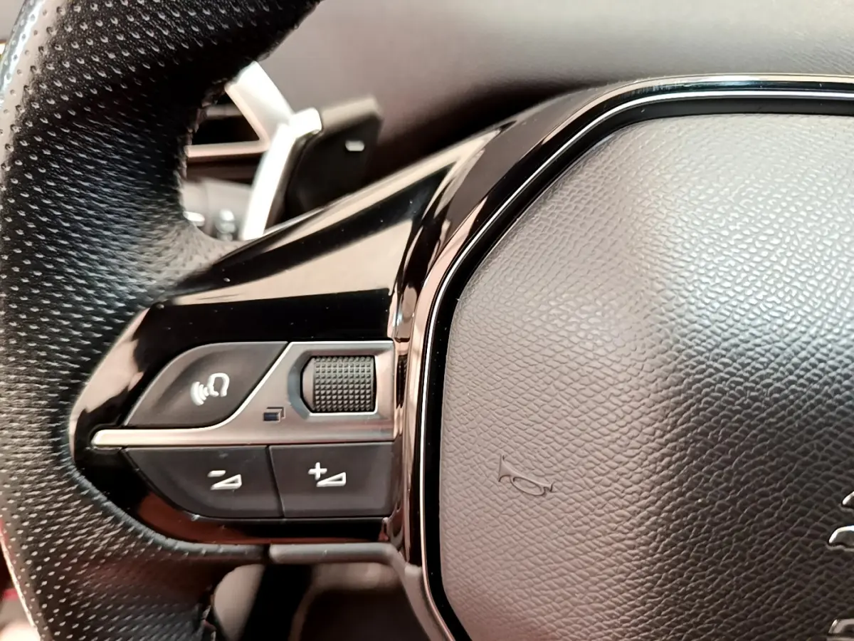 Gros plan sur les commandes gauche du volant cuir perforé du Peugeot 3008 GT rouge, avec boutons multifonctions.