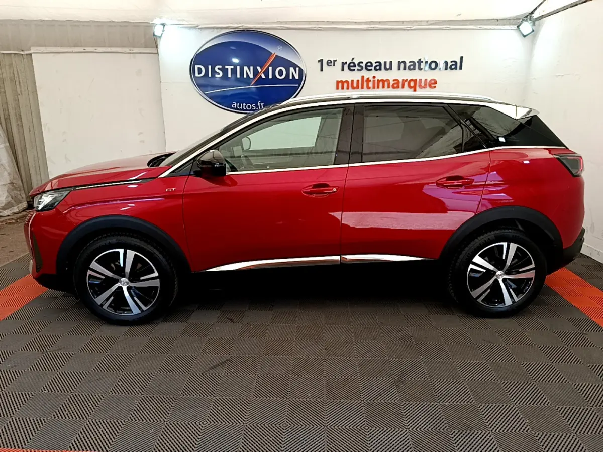 Profil droit d'un Peugeot 3008 GT rouge avec toit noir et jantes alliage bicolores, en intérieur showroom.