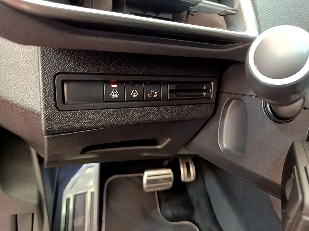 Vue rapprochée des commandes d'assistance à la conduite sur le côté gauche du tableau de bord noir du Peugeot 3008 rouge.