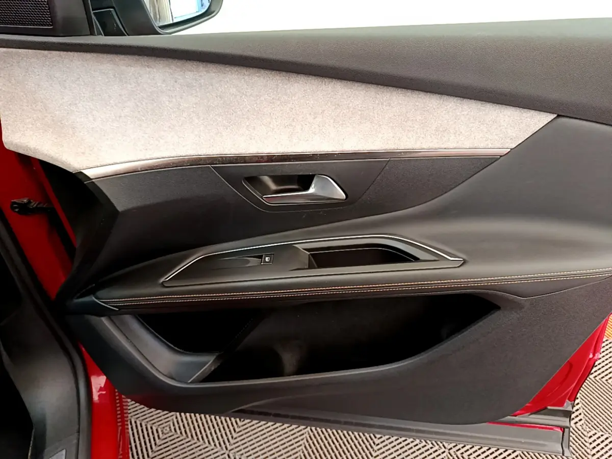 Vue intérieure côté gauche de la porte rouge du Peugeot 3008 GT avec garniture noire et surpiqûres contrastées.