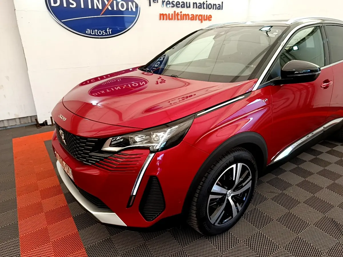 Vue 3/4 avant d'un Peugeot 3008 GT rouge avec phares LED et jantes alliage bicolores dans un showroom.