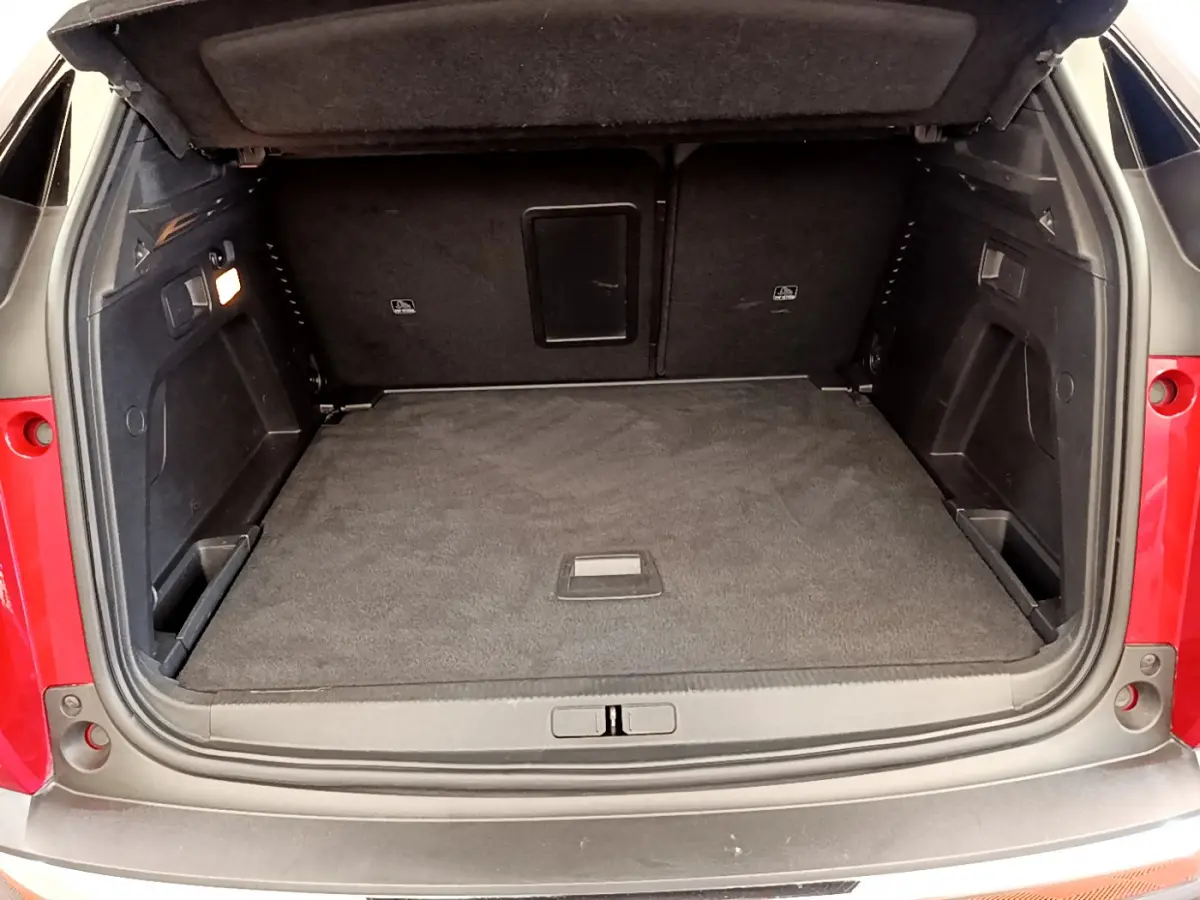 Coffre ouvert vu de l'arrière d'un Peugeot 3008 rouge, espace de chargement propre et bien éclairé.
