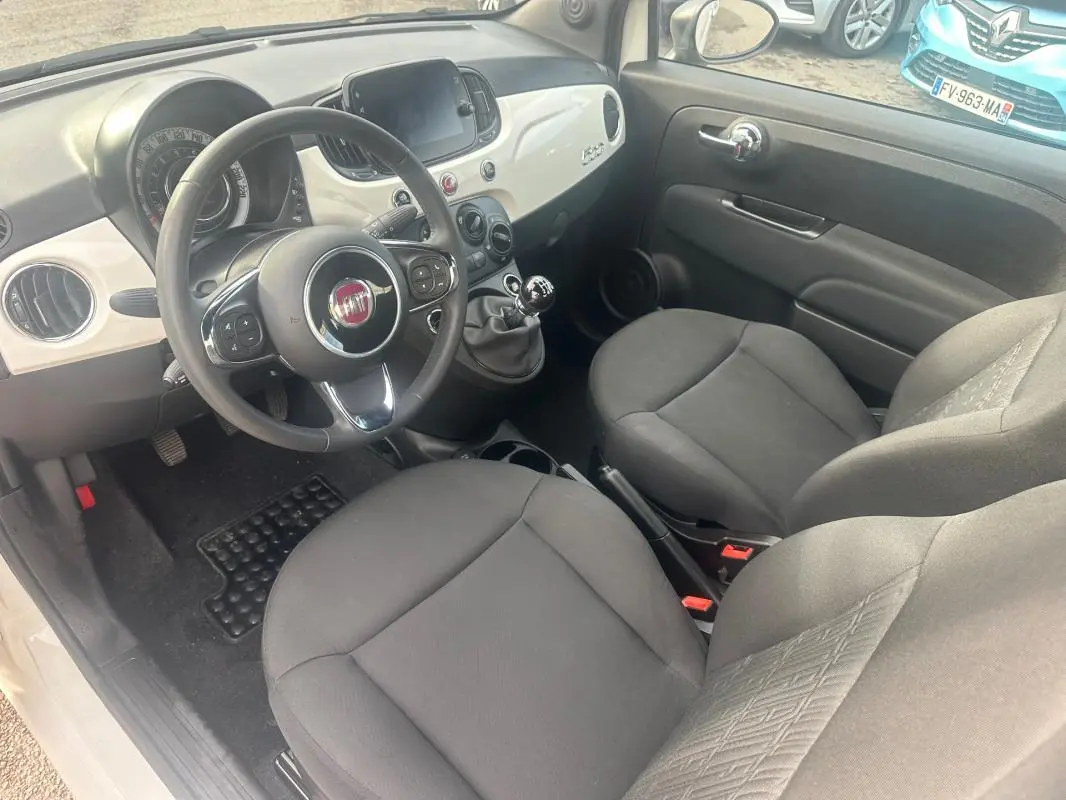Vue intérieure côté conducteur de la Fiat 500 blanche 2023, avec tableau de bord clair et boîte manuelle visible.