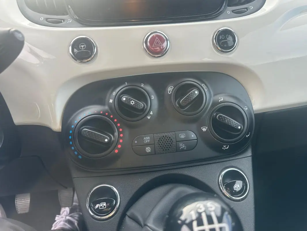 Gros plan sur la console centrale blanche et noire de la Fiat 500 blanche 2023, avec commandes de climatisation et levier de vitesse manuel.