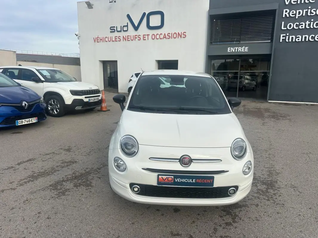 Vue de face d'une FIAT 500 blanche 2023, avec logo FIAT visible et plaque "Véhicule récent" sur un parking de concession.
