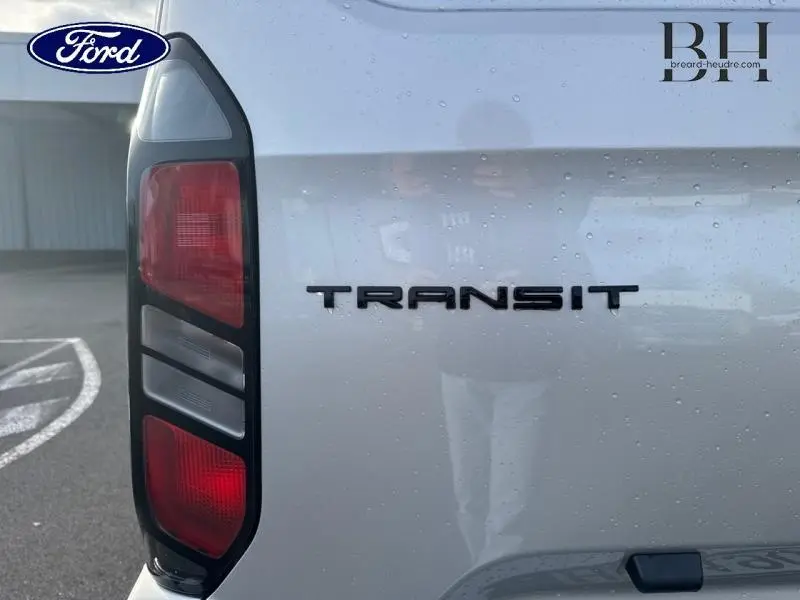 Gros plan sur le feu arrière gauche et le logo Transit du Ford Transit Custom gris lunaire métallisé, avec gouttes d'eau visibles.