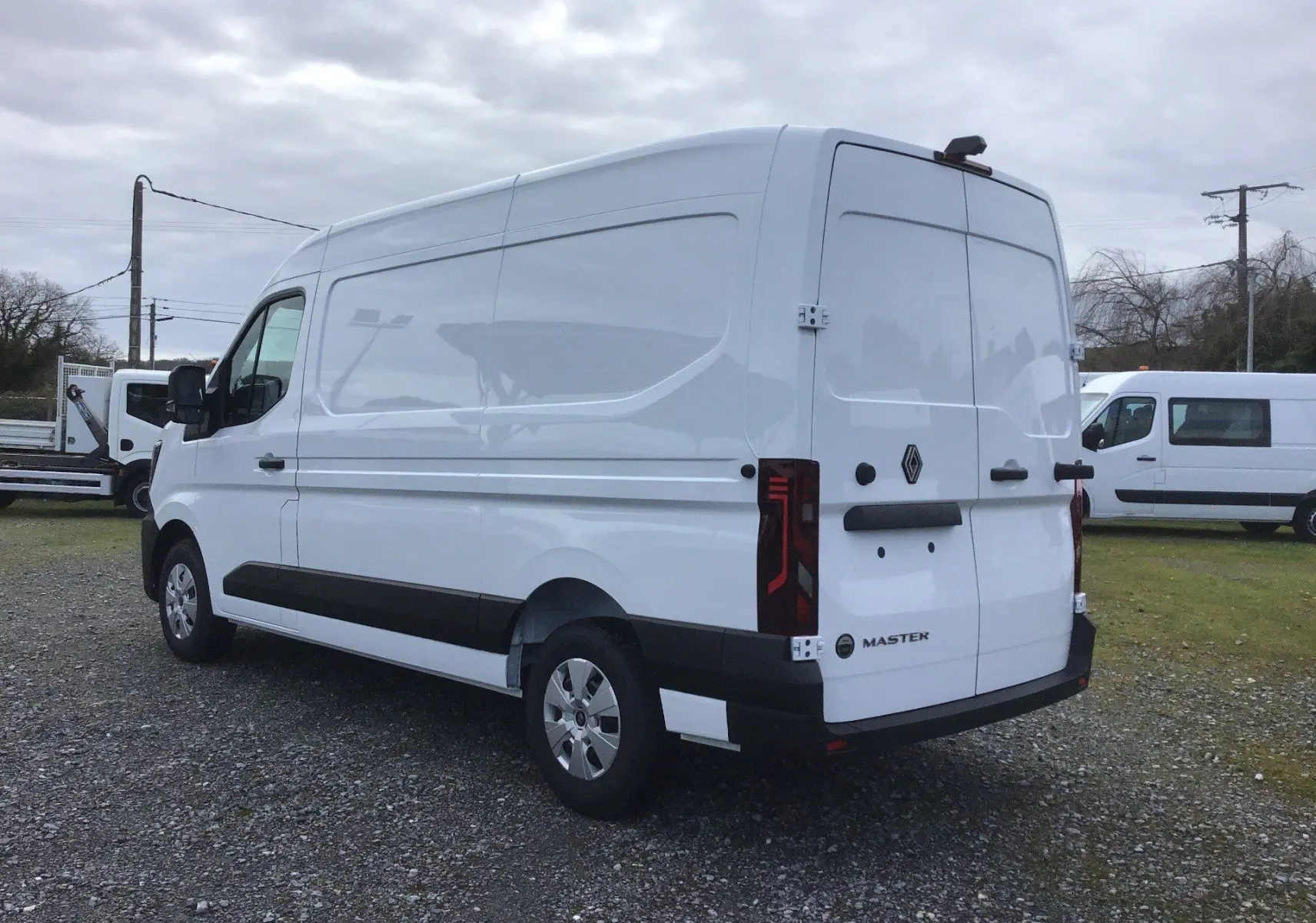 Vue 3/4 arrière droite d’un utilitaire Renault Master blanc avec portes arrière fermées sur un sol gravillonné.
