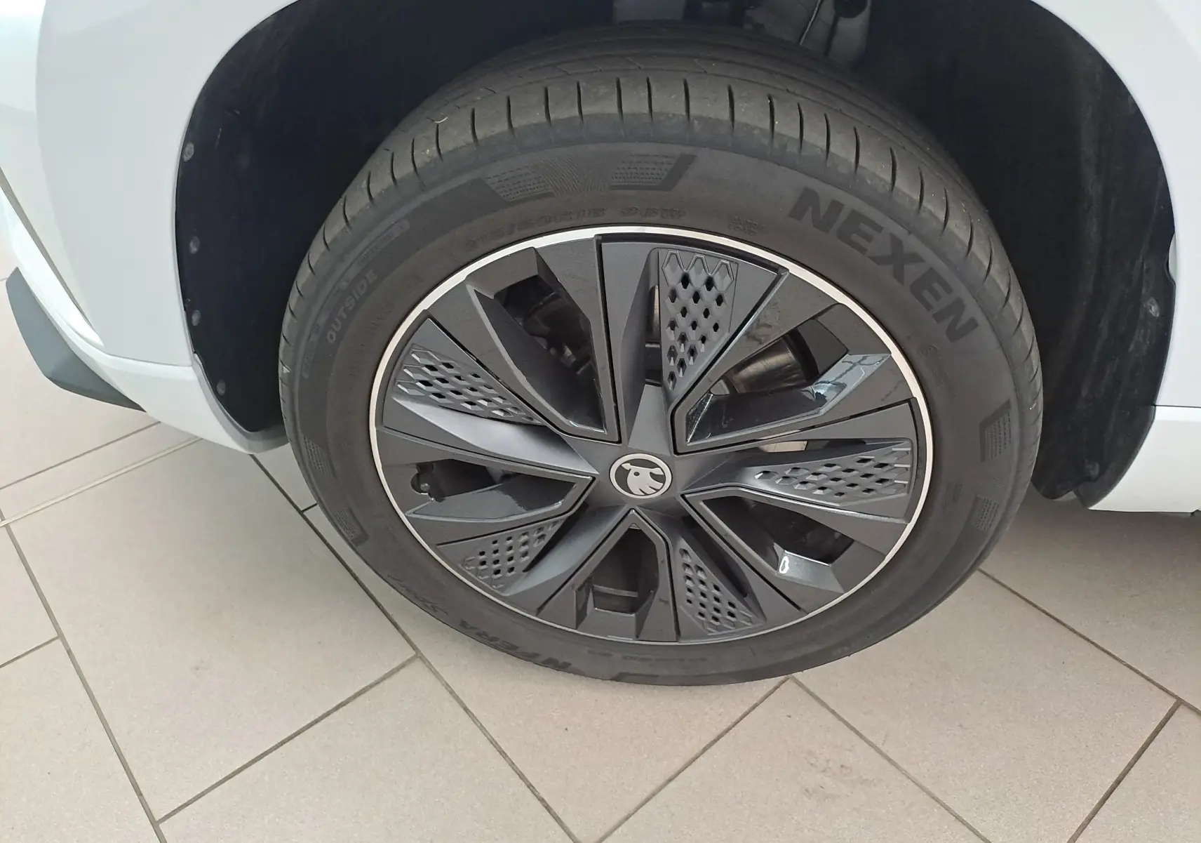 Gros plan sur la roue avant droite d’un Skoda Karoq blanc lune 2025 avec jante noire au design géométrique.