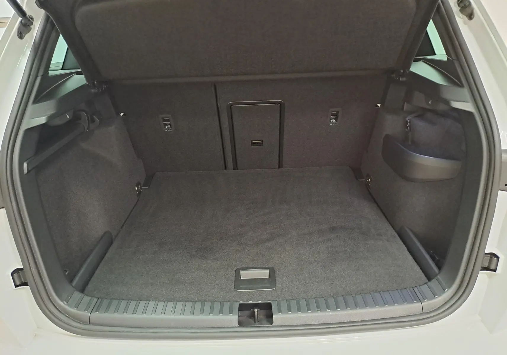 Coffre ouvert d’un Skoda Karoq 2025 blanc lune, vue de l’arrière montrant un espace de chargement spacieux et tapis gris.