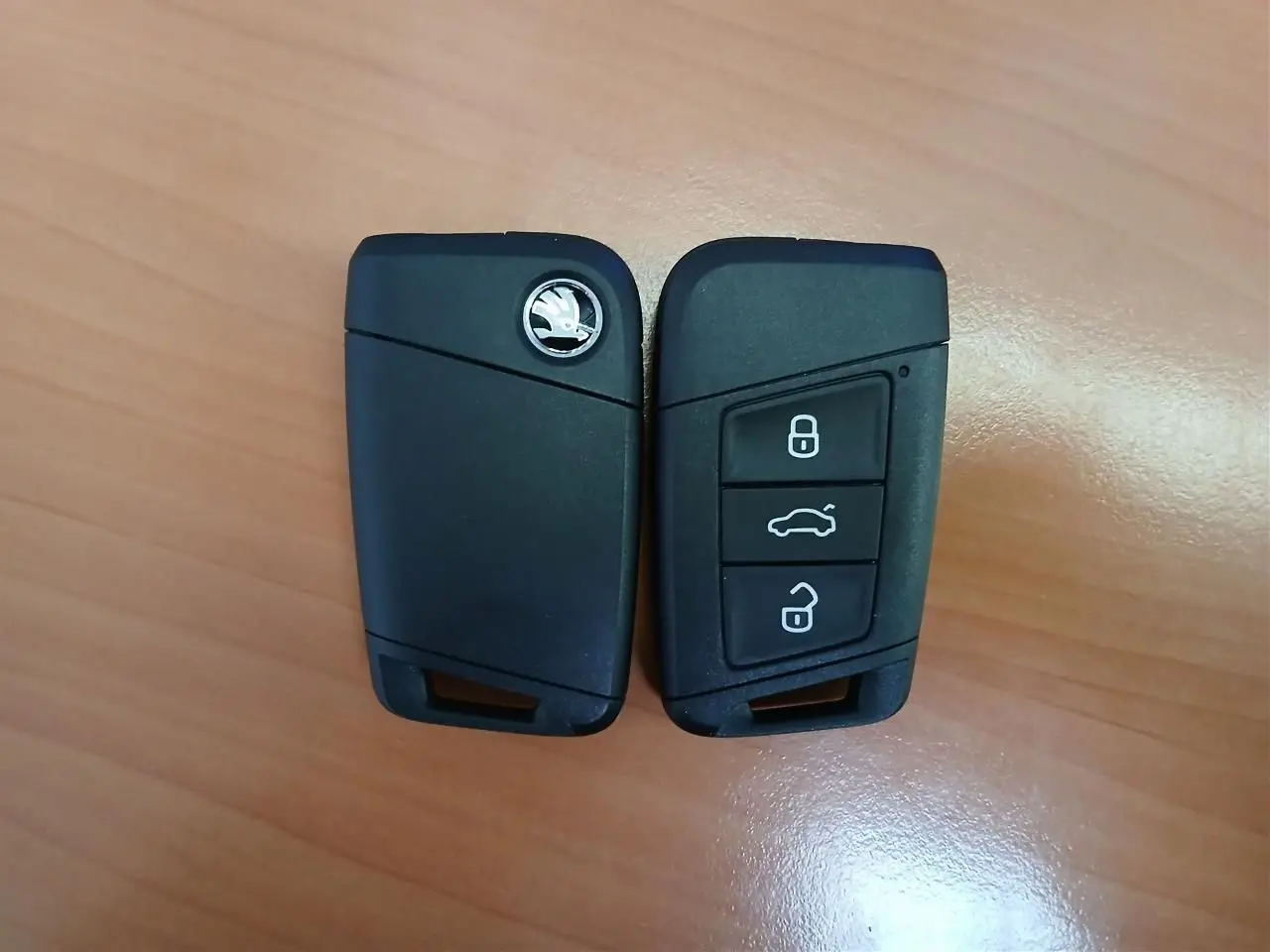 Clé de voiture SKODA KAROQ 1.5 TSI 150 DSG7 SPORTLINE 2025 en noir, vue de face et dos sur fond bois.