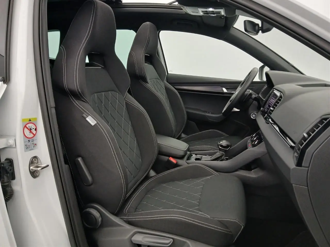 Intérieur du Skoda Karoq 2025 blanc lune, vue côté gauche sur les sièges sport noirs avec surpiqûres blanches.