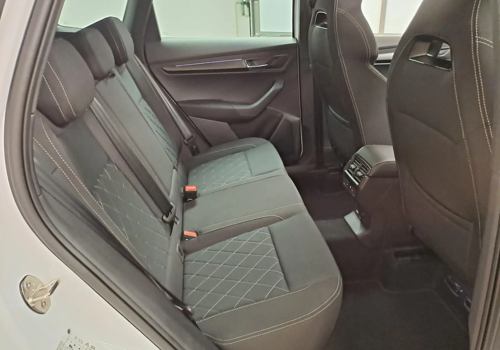 Vue intérieure côté gauche des sièges arrière noirs avec surpiqûres blanches du Skoda Karoq Blanc Lune 2025 Sportline.