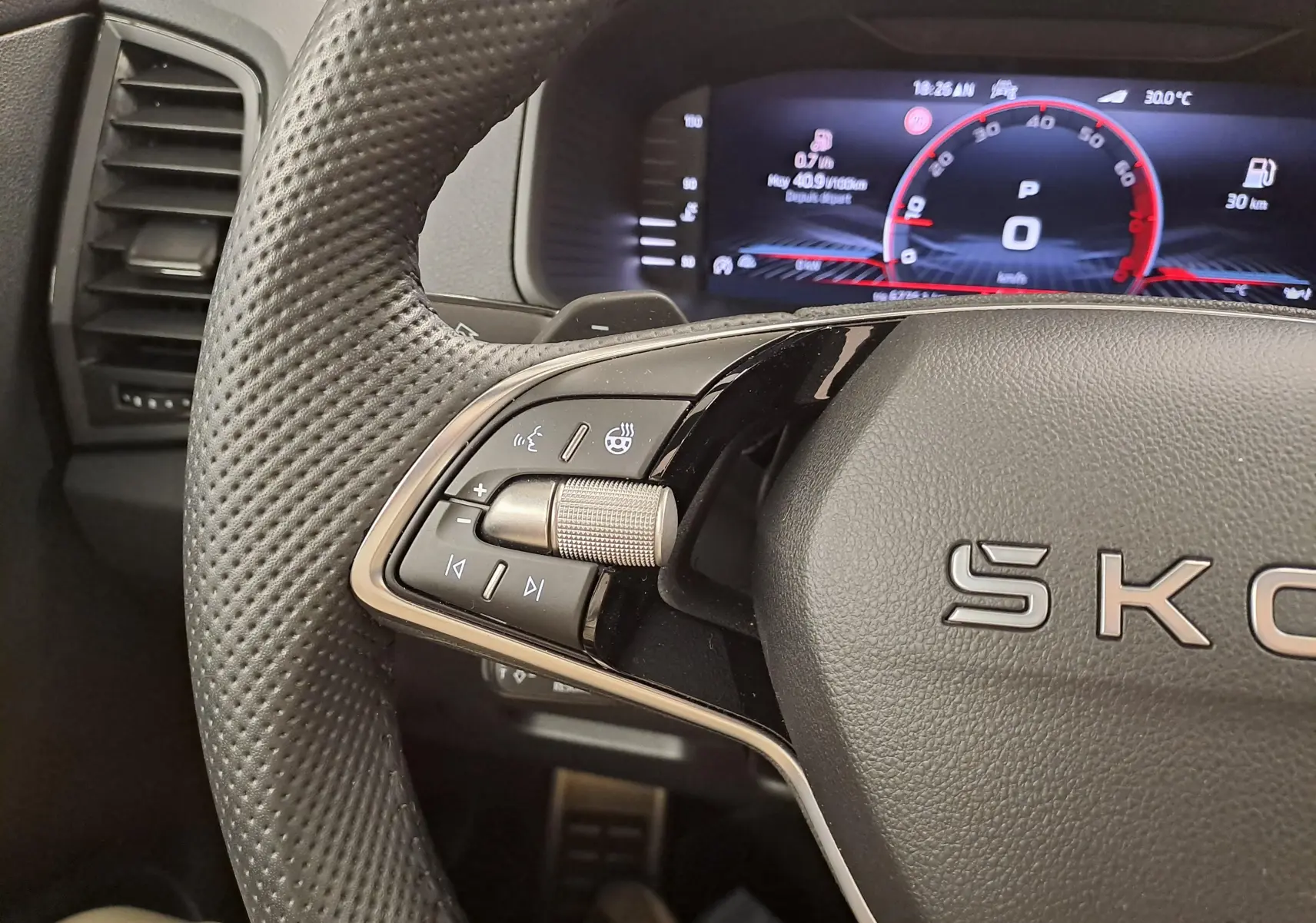 Gros plan sur le volant perforé et les commandes multifonctions du Skoda Karoq 1.5 TSI 150 DSG7 Sportline, tableau de bord numérique visible.