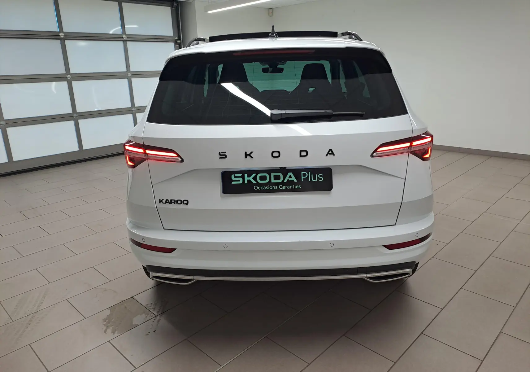 Vue arrière d'un Skoda Karoq blanc lune 2025 avec feux LED allumés et double sortie d'échappement intégrée au pare-chocs.