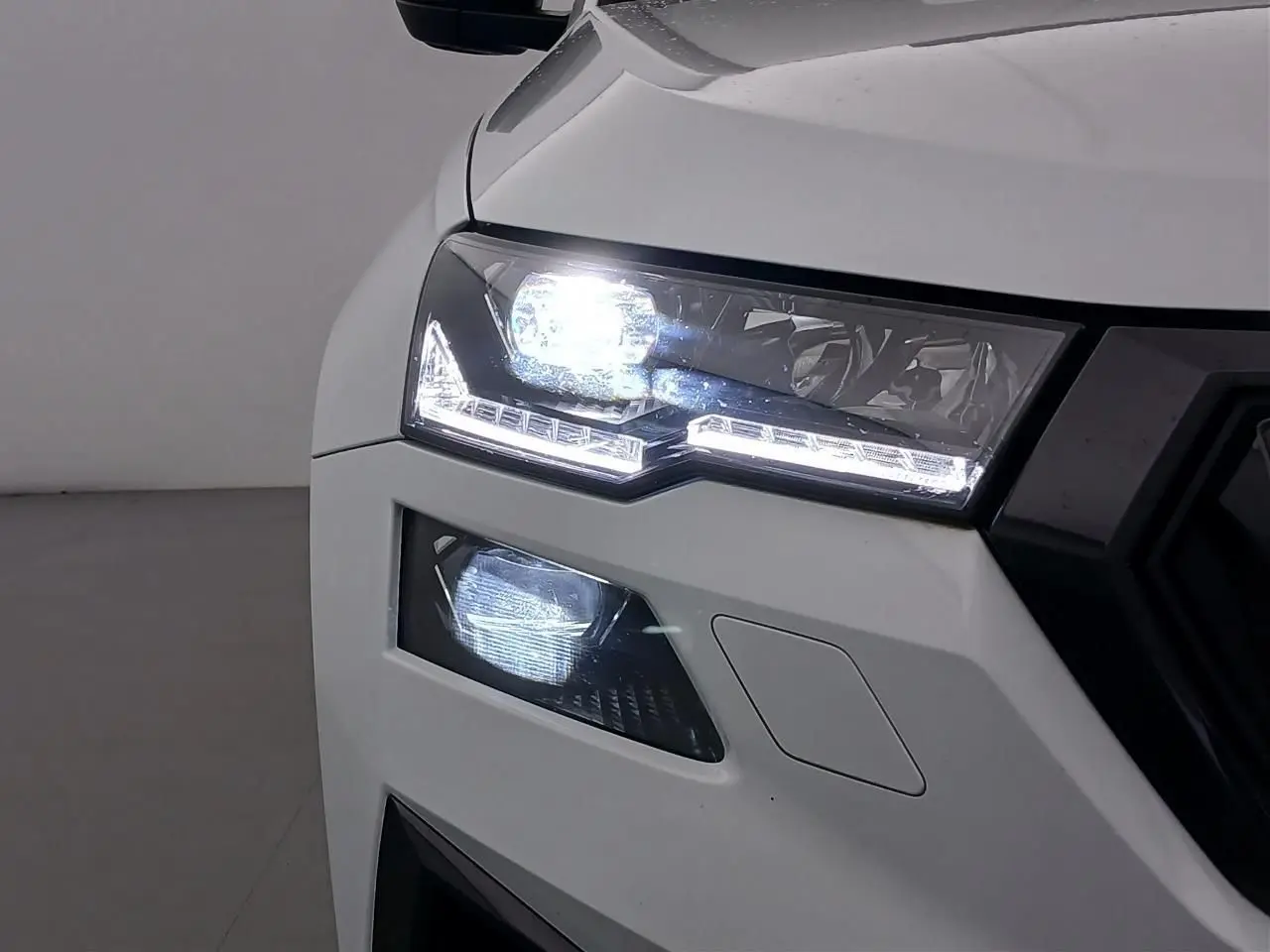 Gros plan sur le phare avant gauche allumé du Skoda Karoq 2025 blanc lune version Sportline.