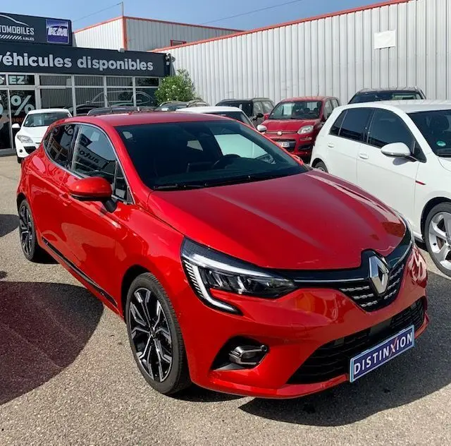 Renault Clio V rouge vue 3/4 avant droit, avec phares LED et jantes alliage distinctives, stationnée en extérieur.