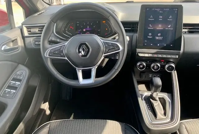 Vue intérieure centrée sur le volant et la console centrale d'une Renault Clio V rouge, avec écran tactile et boîte automatique.