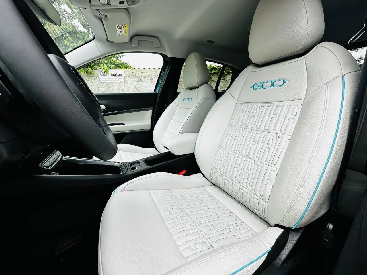Vue intérieure côté conducteur de la FIAT 600 1.2 Hybrid 2024, sièges ivoire avec logo 600 bleu et surpiqûres FIAT.