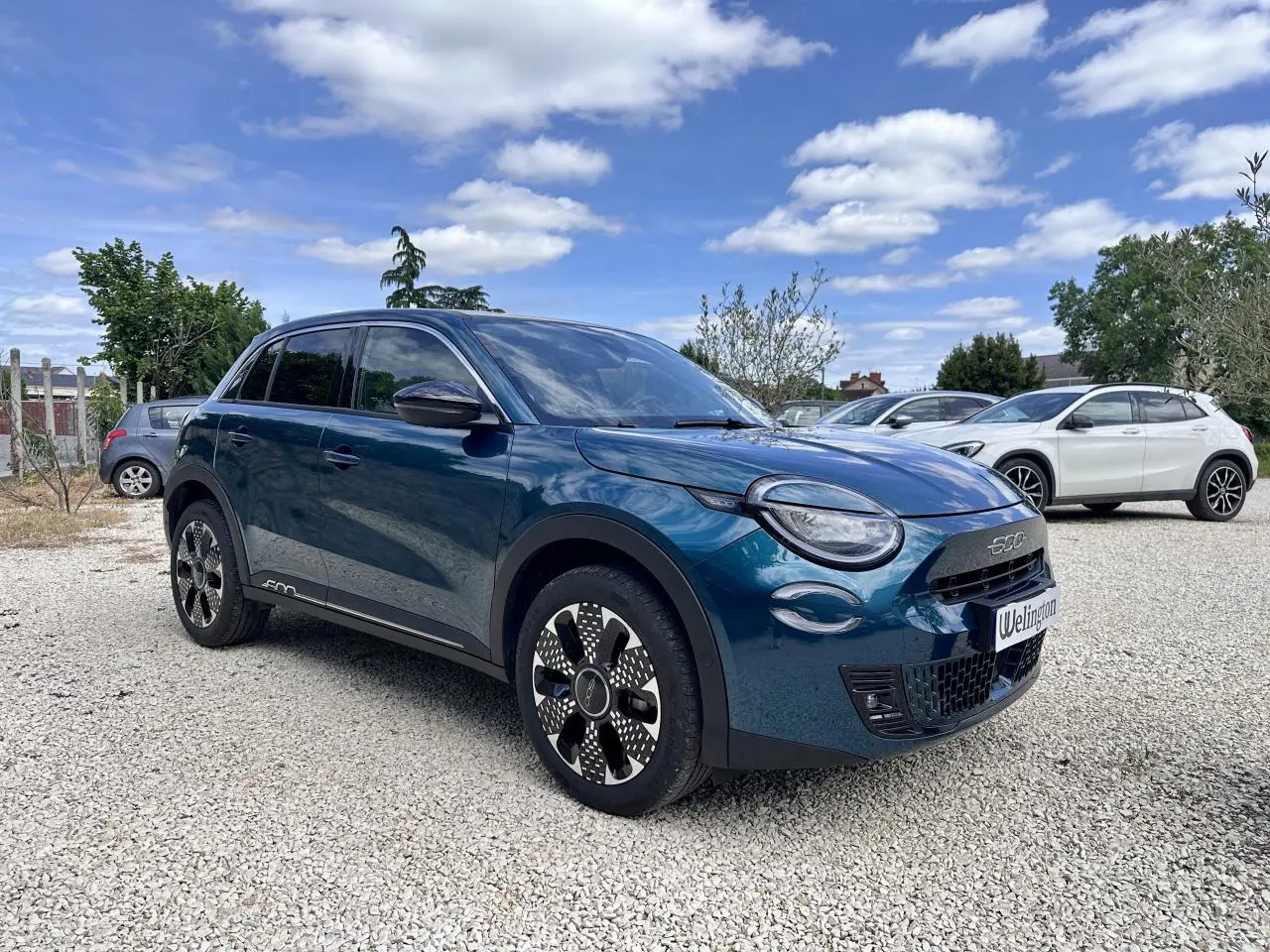 Vue 3/4 avant droite d'une FIAT 600 bleu clair avec jantes stylisées et calandre noire en extérieur.