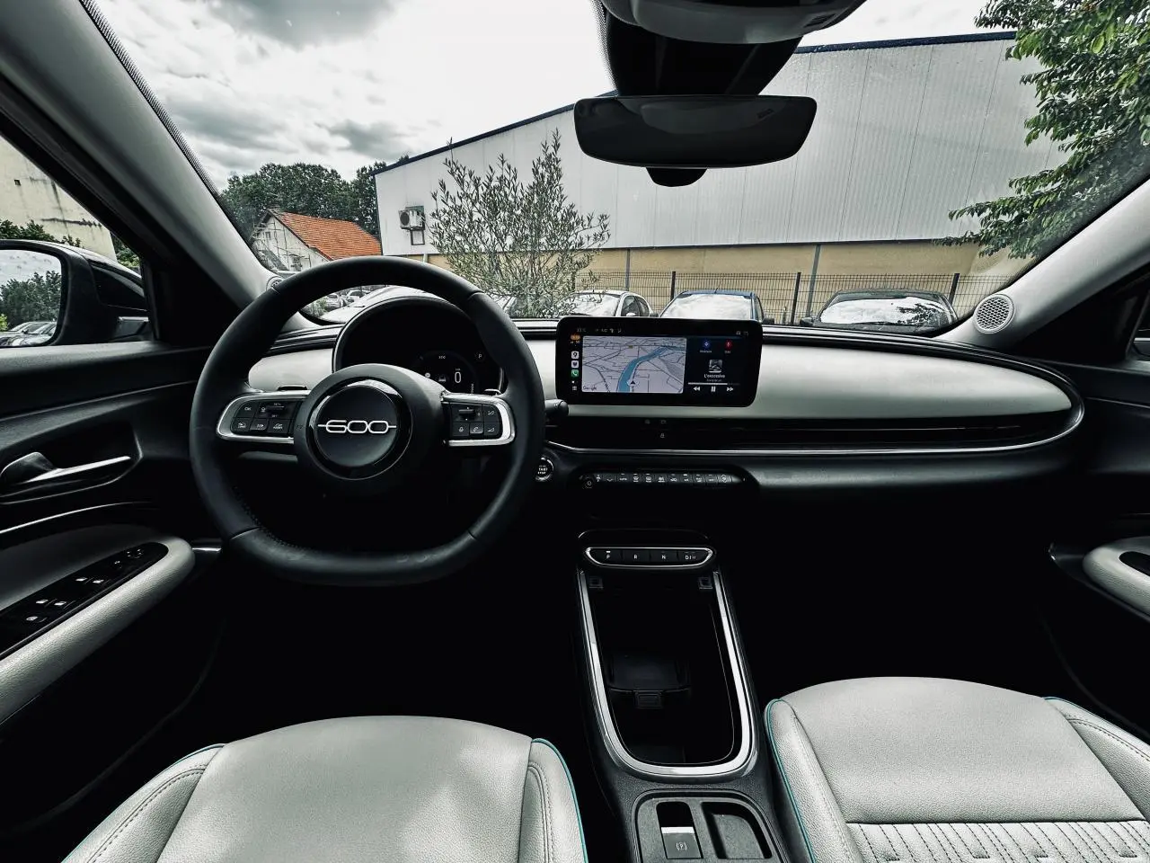 Vue intérieure avant du Fiat 600 La Prima 2024, planche de bord ivoire avec écran tactile et volant marqué 600.