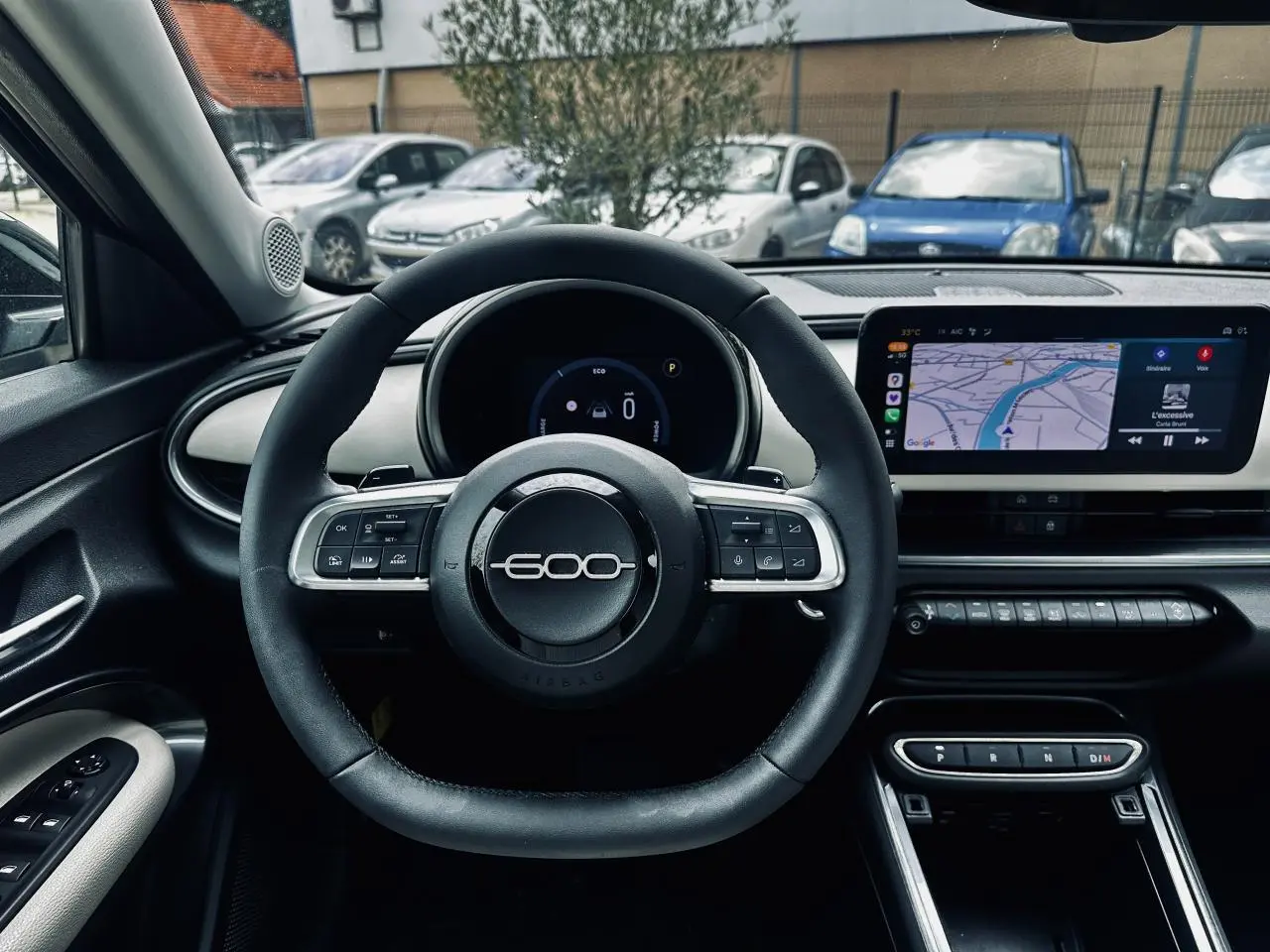 Vue intérieure centrée sur le volant noir marqué 600 et l'écran tactile du tableau de bord de la Fiat 600 bleu clair 2024.