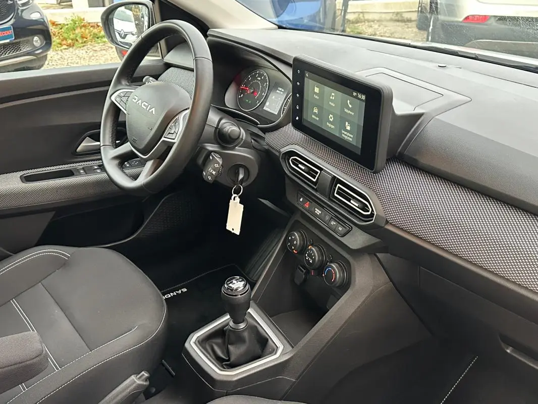 Vue intérieure côté conducteur du tableau de bord noir et gris du Dacia Sandero blanc avec écran tactile et boîte manuelle.