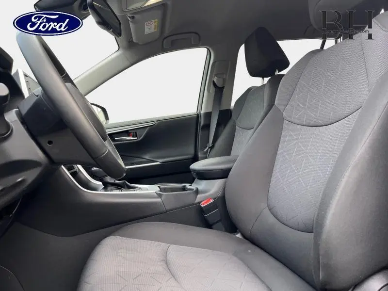 Vue intérieure côté conducteur du Toyota RAV4 2022, sièges tissu noir avec motifs géométriques et accoudoir central.