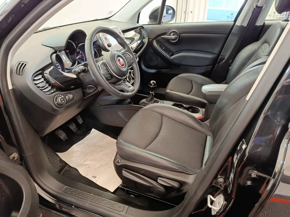Vue intérieure côté conducteur de la Fiat 500X 2020, sièges noirs, volant multifonctions et levier de vitesse manuel visibles.