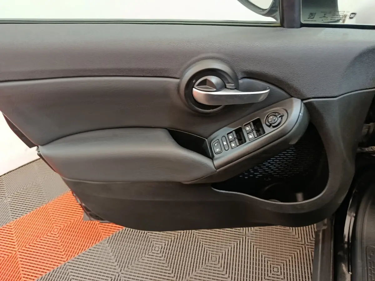 Gros plan sur la porte intérieure côté conducteur noire de la Fiat 500X avec commandes des vitres et poignée argentée.