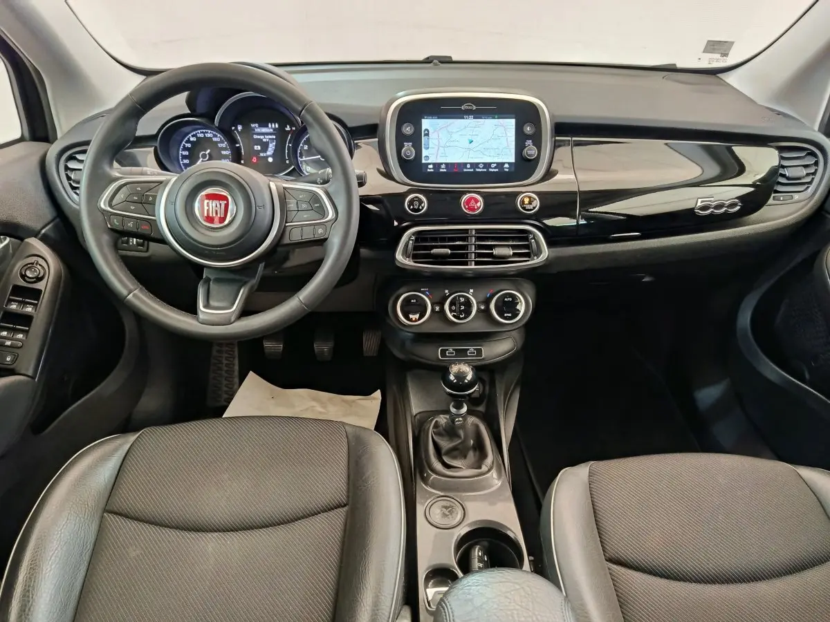 Vue intérieure avant du tableau de bord noir brillant et volant cuir de la Fiat 500X 2020 avec écran tactile et boîte manuelle.