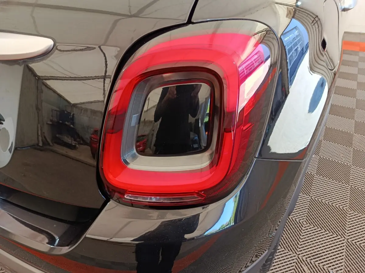 Gros plan sur le feu arrière droit rouge et noir d’un FIAT 500X noir, avec reflet de l’environnement.