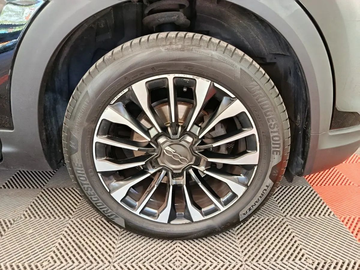 Gros plan sur la roue avant droite avec jante alliage noire et argentée du FIAT 500X blanc.