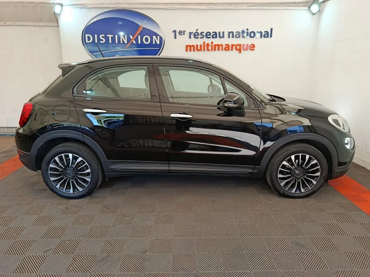 Vue latérale droite d'un FIAT 500X noir 2020 avec jantes alliage et rails de toit noirs en intérieur showroom.