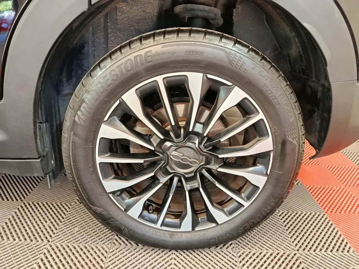 Gros plan sur la roue avant droite de la Fiat 500X blanche, avec jante alliage noire et argentée distinctive.