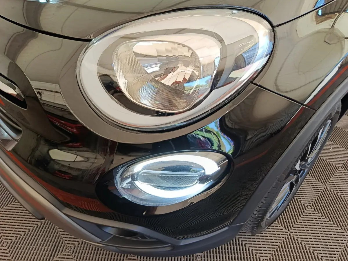 Gros plan sur le phare avant droit et le feu antibrouillard d’un Fiat 500X noir, détails chromés visibles.