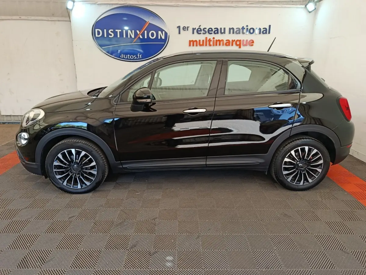 Profil côté gauche d'un FIAT 500X noir avec jantes alliage et toit noir, en intérieur sur sol damier.