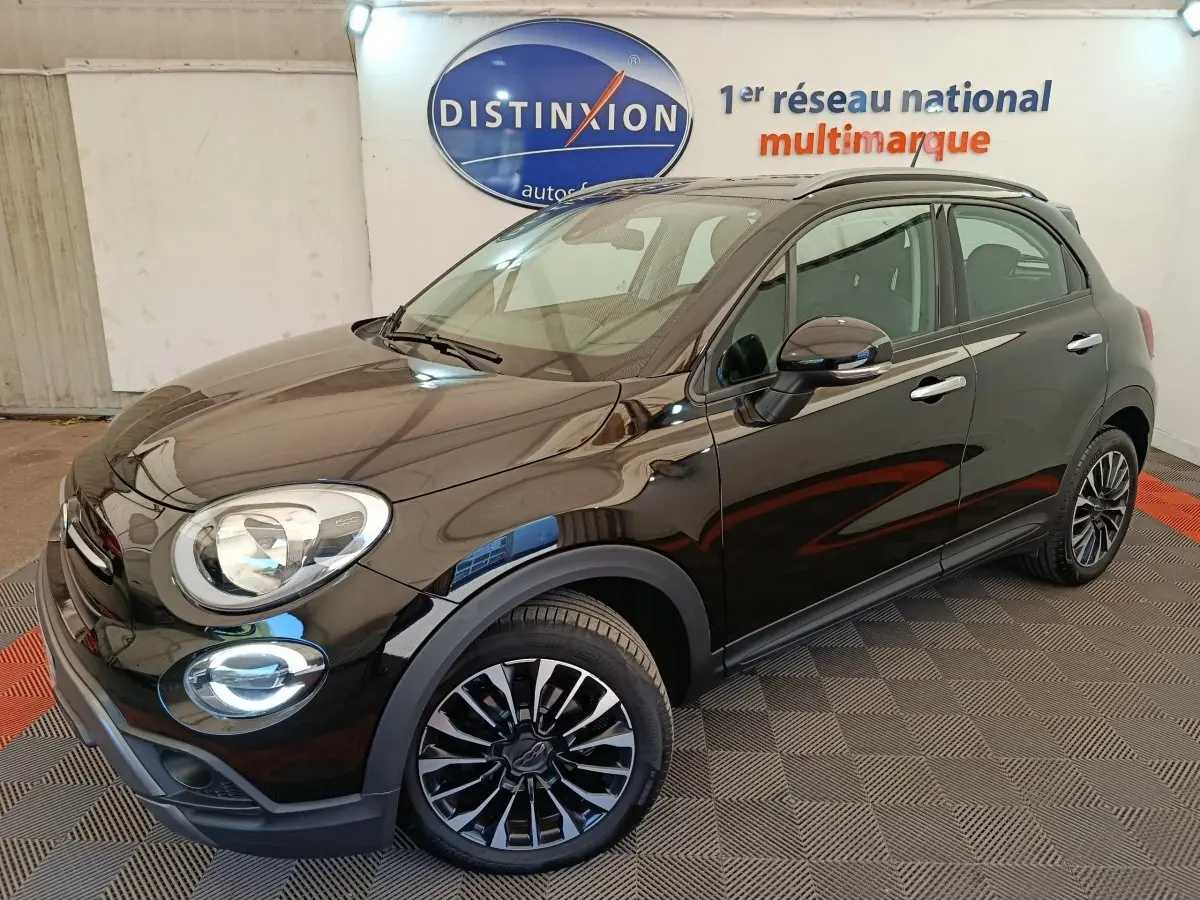 Vue 3/4 avant droit d'une FIAT 500X noire avec jantes alliage et toit ouvrant en intérieur showroom.