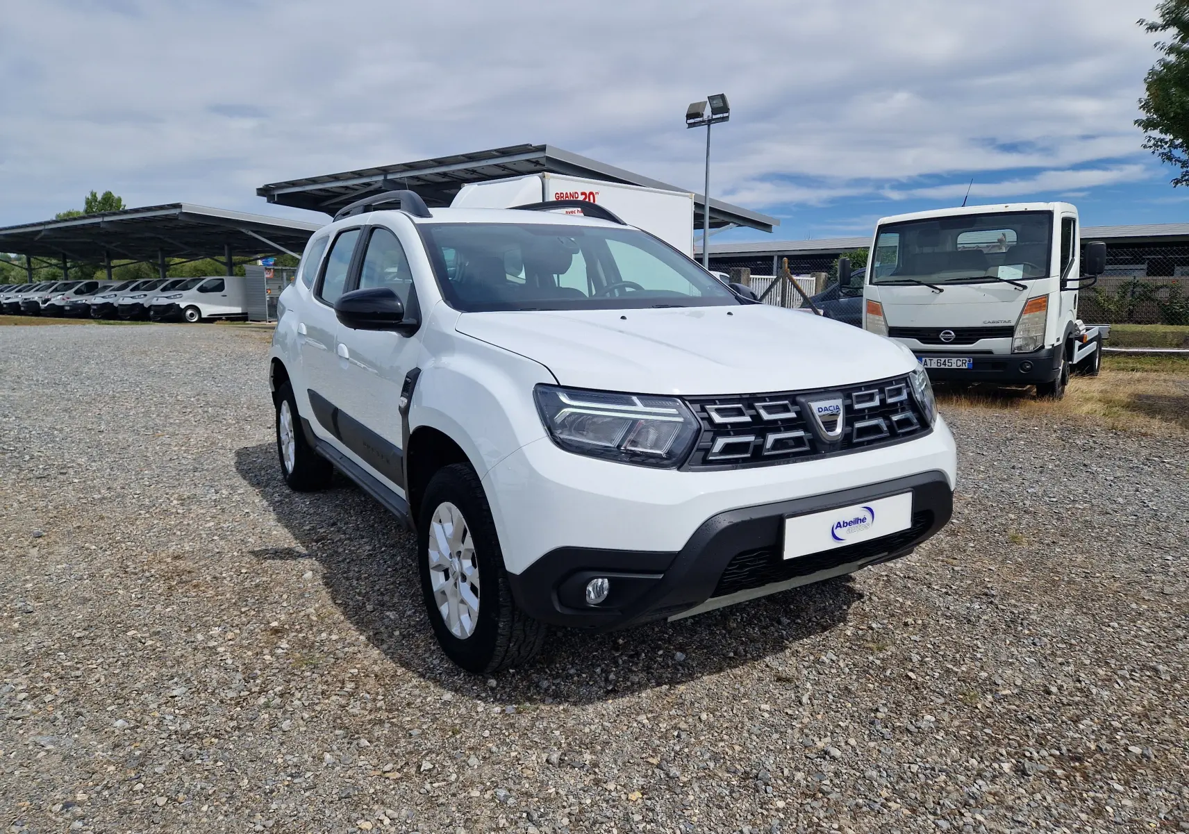 Dacia Duster blanc en 3/4 avant droit, SUV compact avec calandre noire et protections latérales noires.
