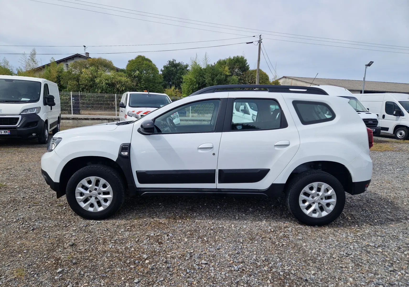 Vue de profil côté gauche d'un Dacia Duster blanc 4x4 avec protections noires et jantes alliage 16 pouces.