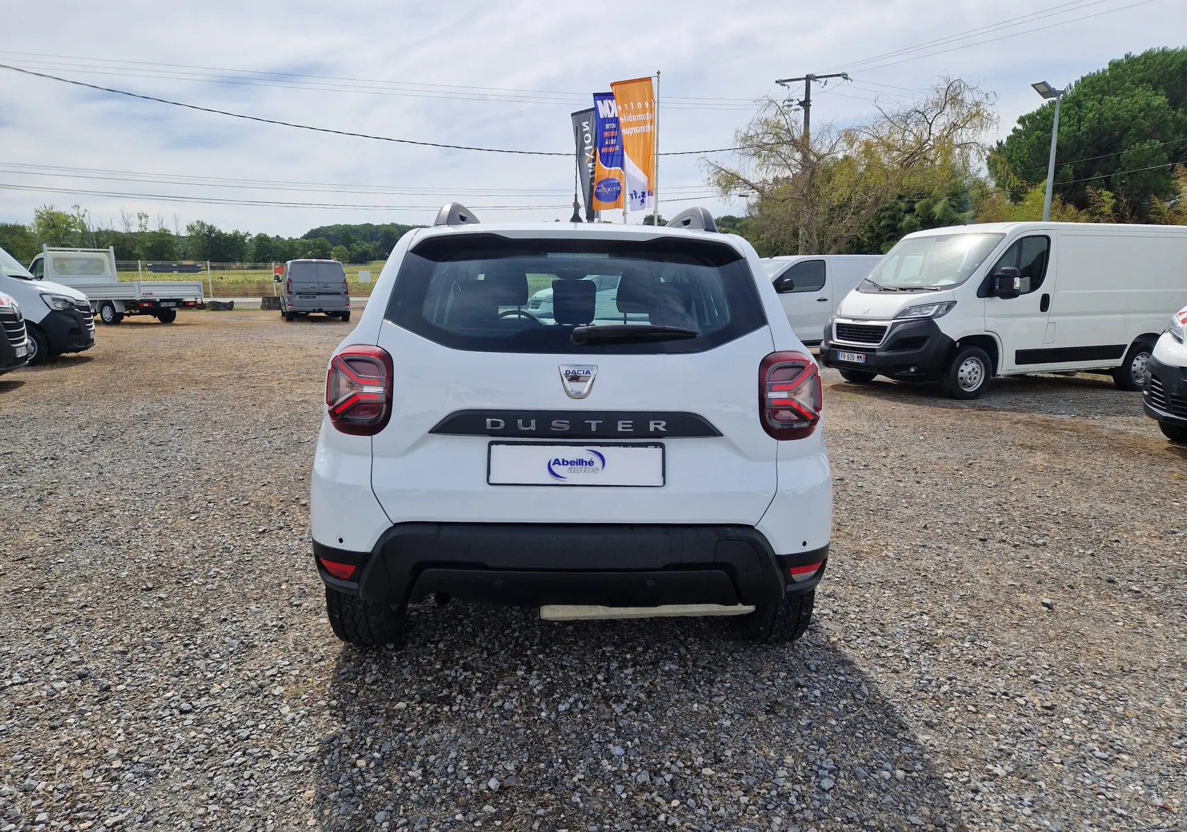 Vue arrière d'un Dacia Duster blanc 2022, avec logo et nom du modèle bien visibles sur un terrain gravillonné.