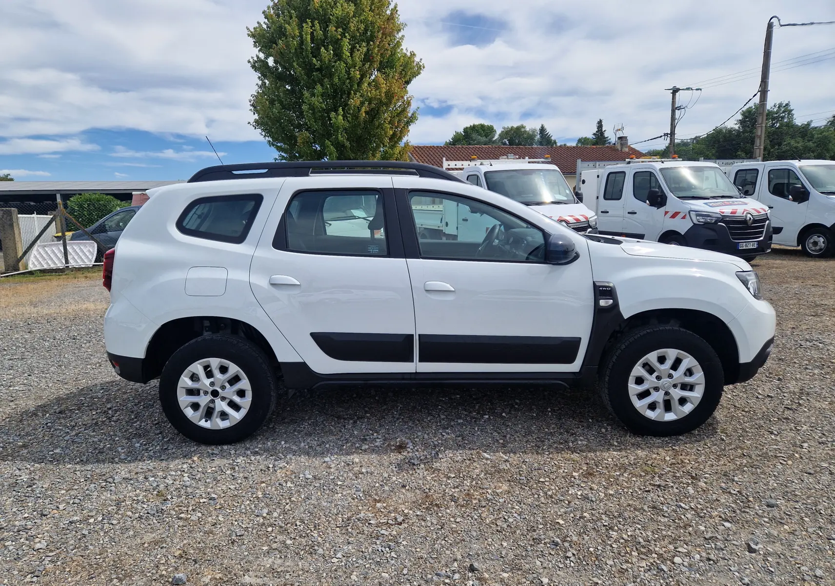 Profil côté gauche d'un Dacia Duster blanc 4x4 2022 avec protections noires et jantes alliage 16 pouces.