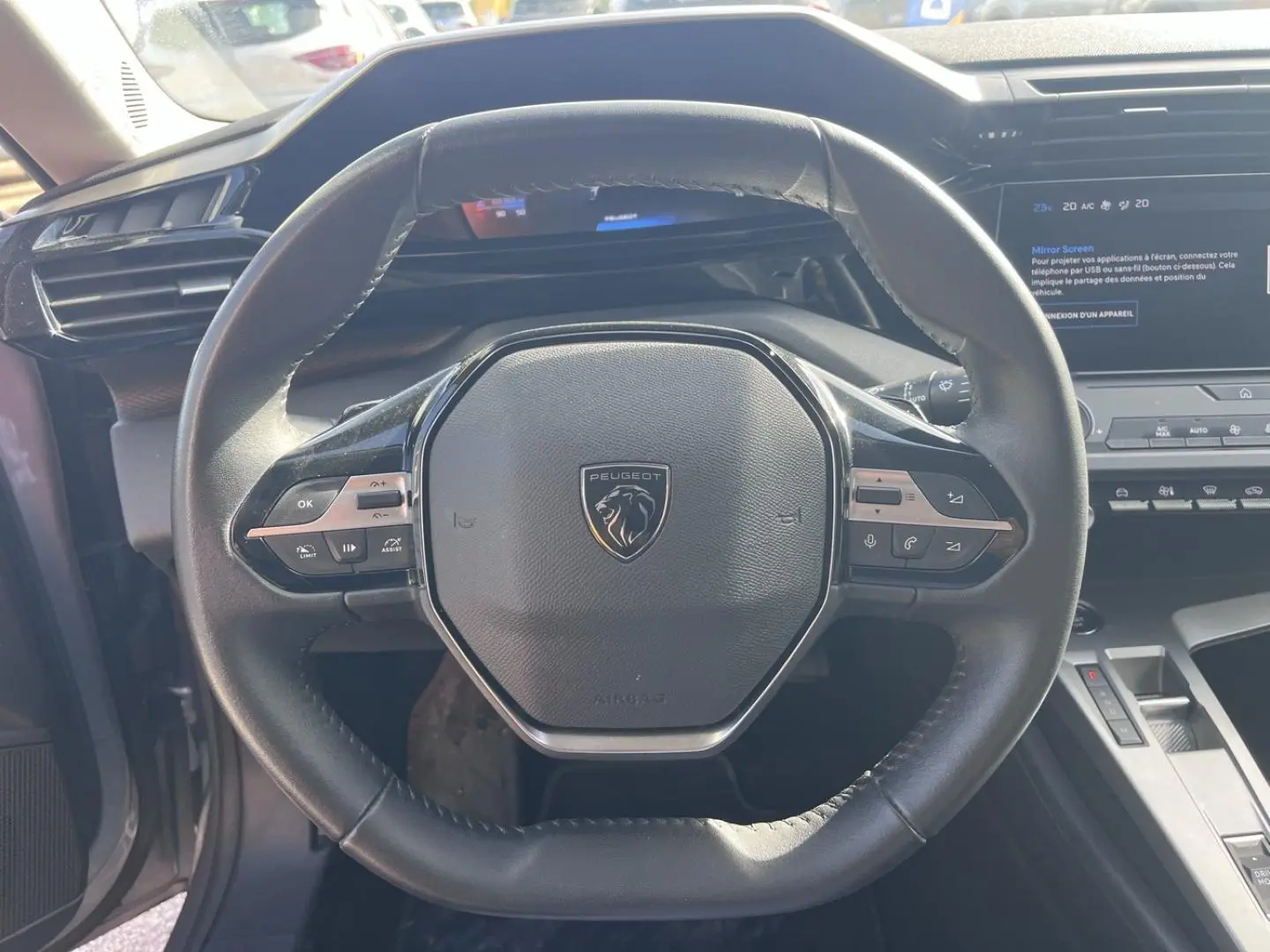 Vue rapprochée du volant multifonction noir de la Peugeot 308 2024 avec tableau de bord et écran tactile en arrière-plan.
