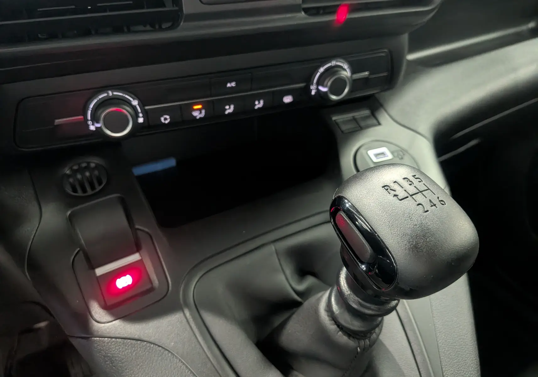 Gros plan sur le levier de vitesses manuel noir et la console centrale du Citroën Berlingo blanc, avec commandes climatisation et frein à main électrique.